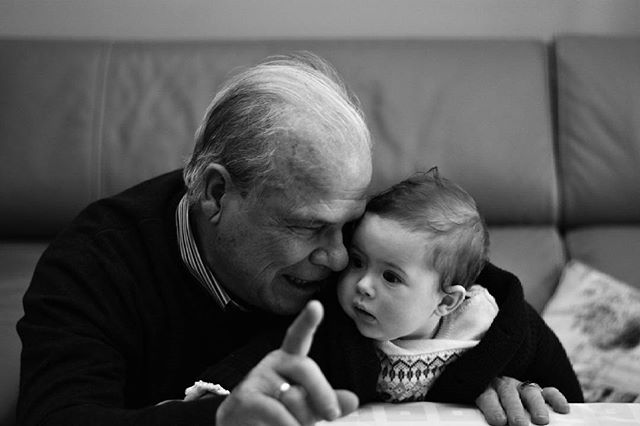 A grandfather lovingly holds his grandchild in a tender moment, showcasing the bond between generations in a classic black and white portrait.
