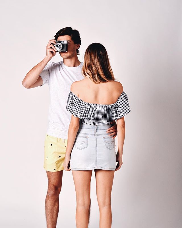 A couple poses in a studio, the man is taking a photo of the woman with a vintage camera.