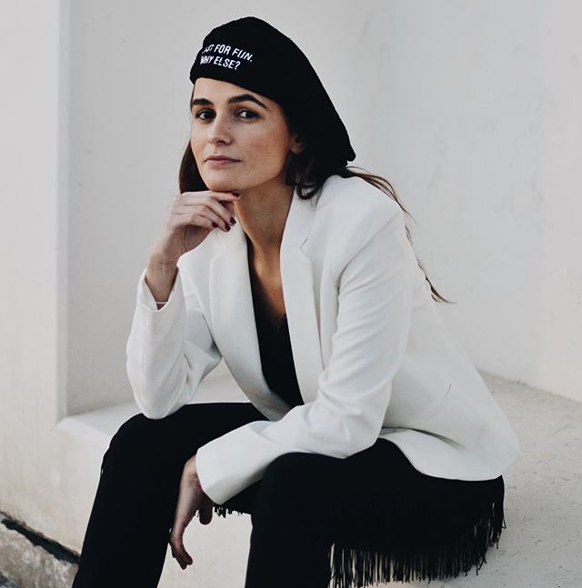 A stylish woman poses in a white blazer and black beret for a fashion editorial.