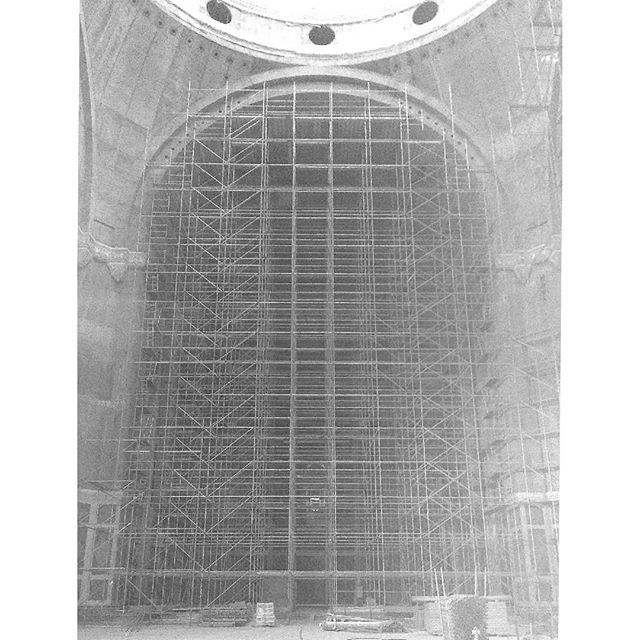 A black and white shot of scaffolding erected inside a large building under construction, reaching up to a dome.