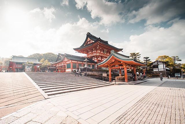 Traditional Japanese shrine architecture with detailed red and white accents, set against a partly cloudy sky.