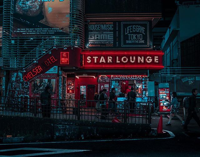 A vibrant Tokyo storefront featuring the Star Lounge and Chelsea Hotel illuminated by neon lights at night.