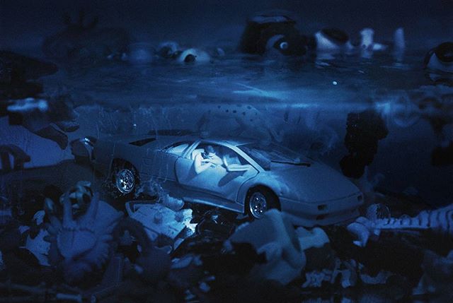 A toy sports car is submerged among other toys in an underwater, surreal, and moody setting.