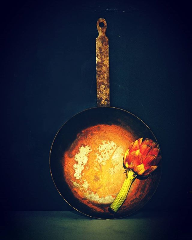 An artichoke rests in a rustic frying pan, bathed in soft, natural light, perfect for a food blog or restaurant menu.