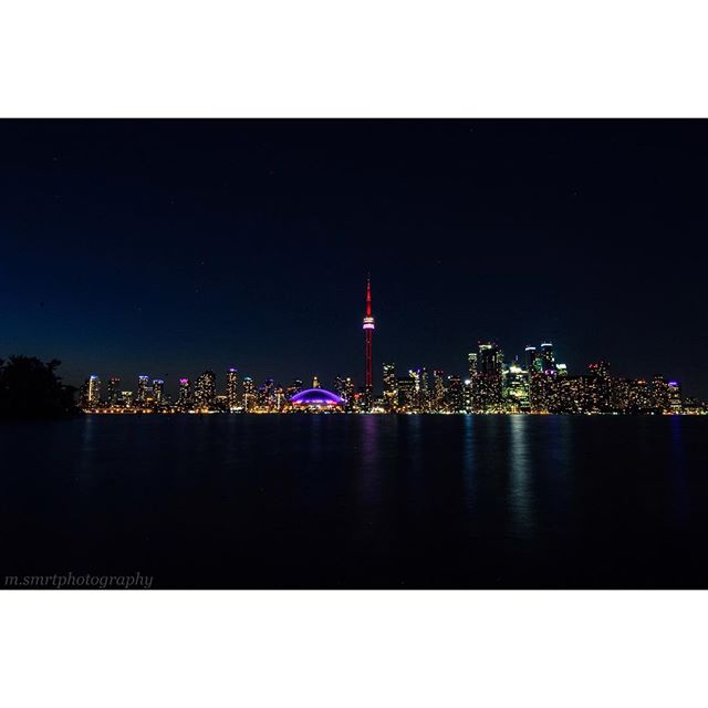 A vibrant cityscape at night, featuring the illuminated CN Tower and Rogers Centre along the waterfront.