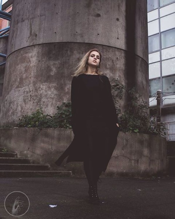 A woman in a black dress walks on a city street with a modern, minimalist aesthetic.