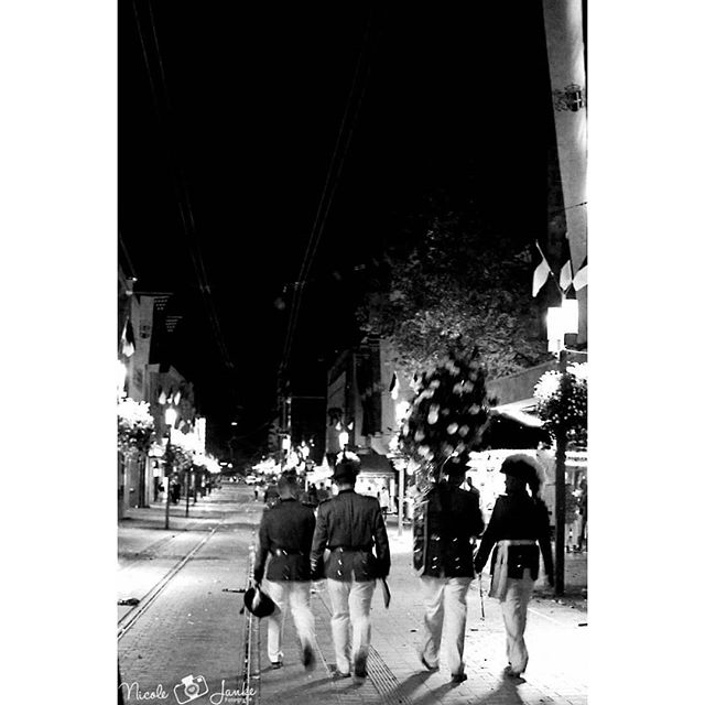 Four men in uniform walk down a street at night in black and white, creating a sense of mystery.