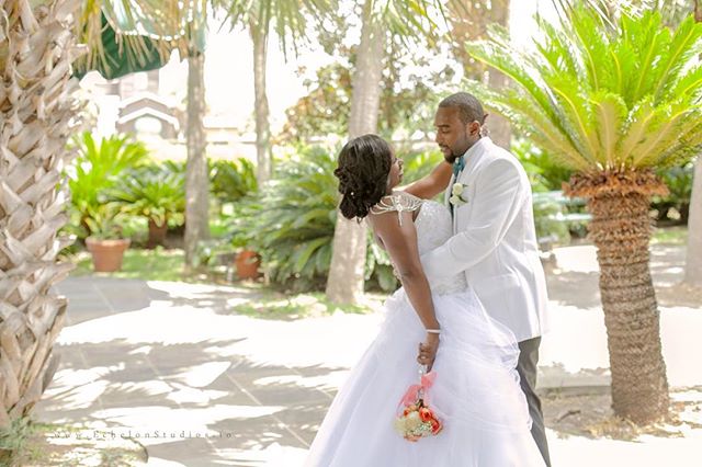 A bride and groom embrace in a garden, surrounded by palm trees on their wedding day.