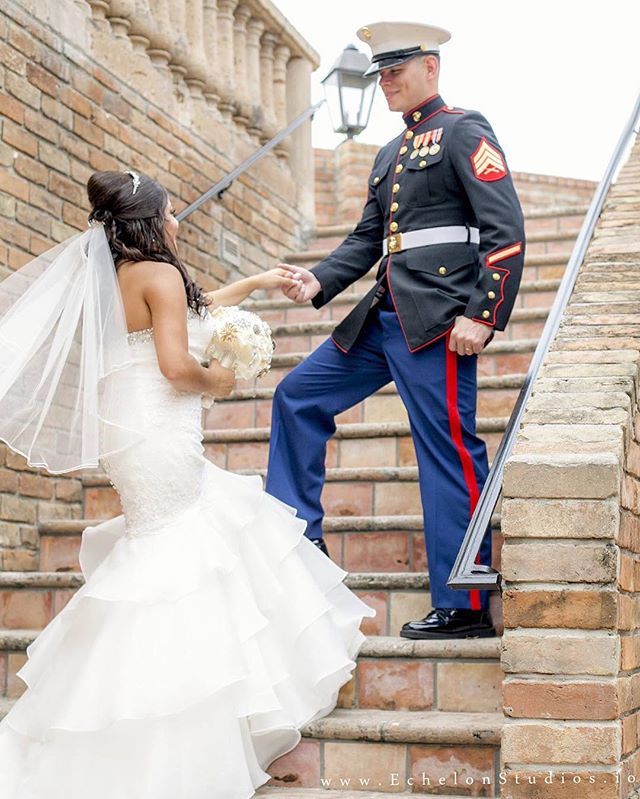 A bride and groom on their wedding day, walking down stairs. The groom is in military uniform.