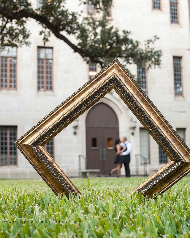 A couple embraces within a golden picture frame on a lawn, creating a romantic wedding moment.