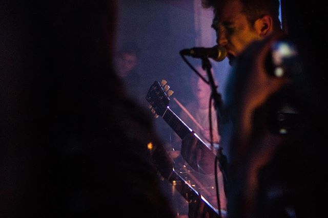 A musician sings into a microphone while playing the guitar during a live concert performance.