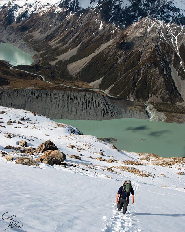 A man hikes up a snow-covered mountain overlooking a lake.