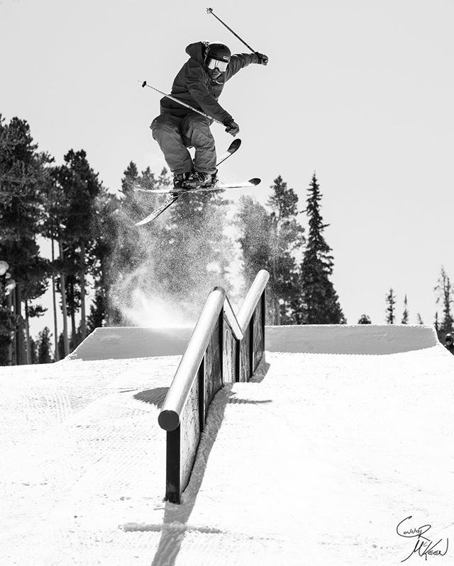A skier performs a trick over a rail in black and white.