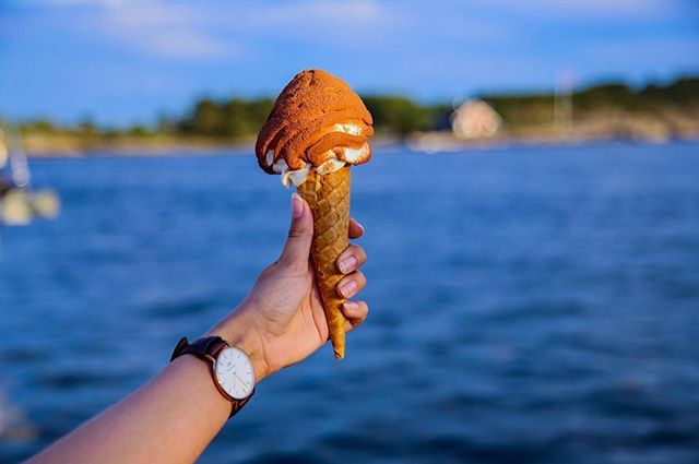 Hand holding a delicious ice cream cone against a beautiful blue water backdrop on a sunny day.