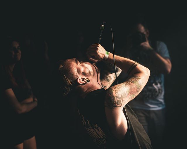 A man intensely sings into a microphone on a dark stage, showcasing emotion through his performance.