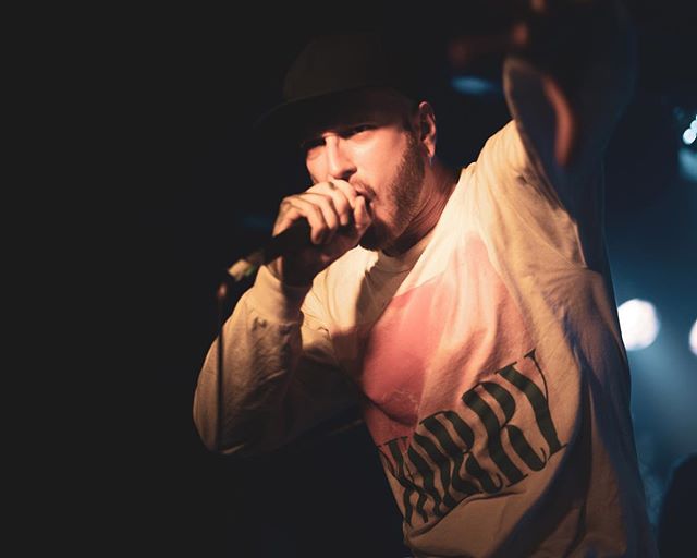 A rapper energetically performs on stage in a concert hall with a microphone in hand.