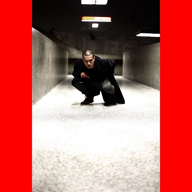 A man in a coat squats in a dimly lit tunnel, creating a moody, urban scene.