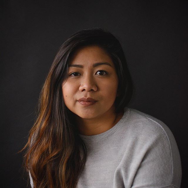 A woman with long brown hair poses for a portrait in front of a dark background.
