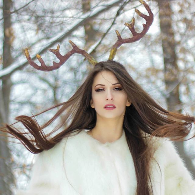A woman with reindeer antlers headdress in a white fur coat in a winter forest.
