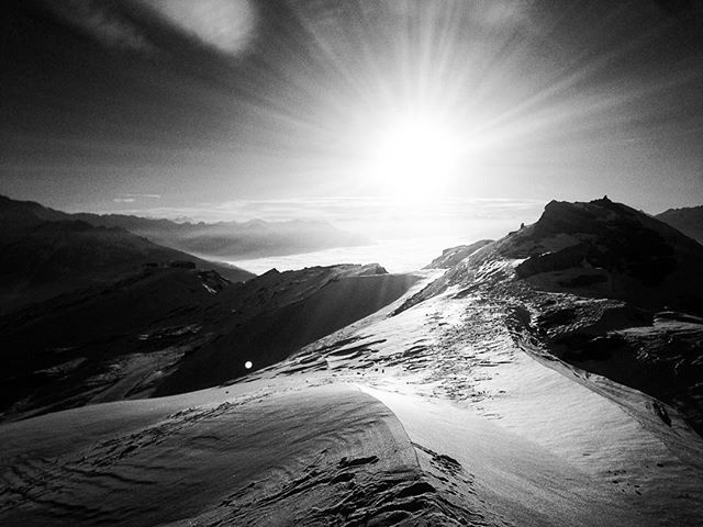 A monochrome shot of a mountain summit covered in snow with a brilliant sunburst, capturing a serene and motivational scene.