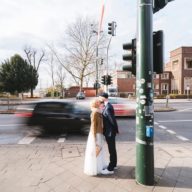 A bride and groom share a kiss on a city street corner by a traffic light, captured with motion blur.