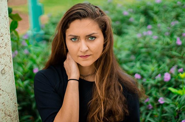 Portrait of a young woman with long brown hair posing in a park.
