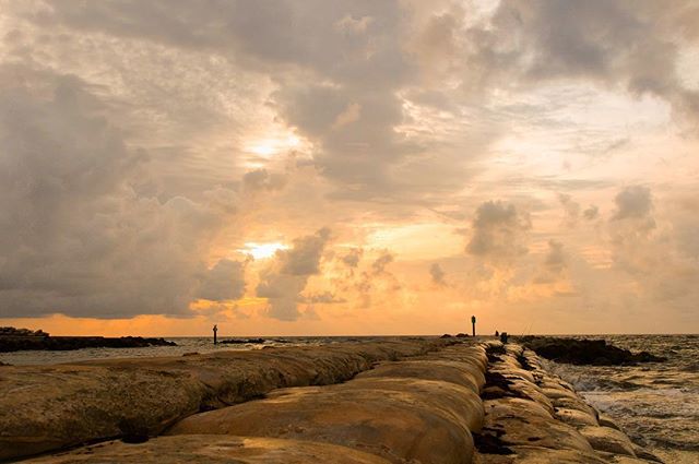 A scenic view of a pier stretching into the sea under a cloudy, golden sky, perfect for travel and relaxation themes.