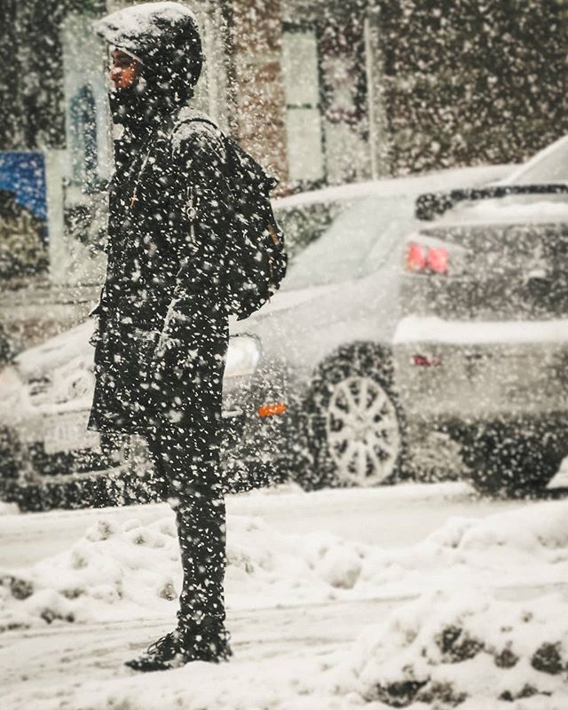 A man walks on a snow-covered city street during a winter storm, showcasing an urban lifestyle.