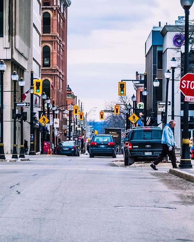 A man crosses a quiet city street lined with buildings and vintage-style street lights.