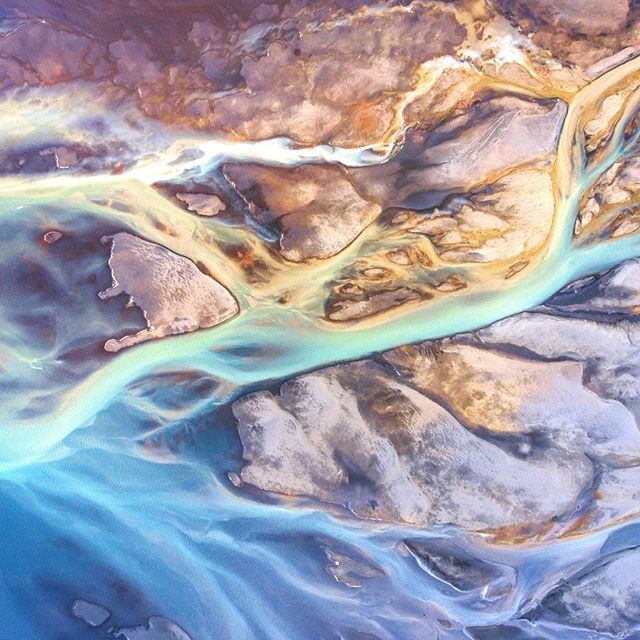 An aerial view showcases the intricate patterns of a glacial river flowing through a rugged landscape in Iceland.