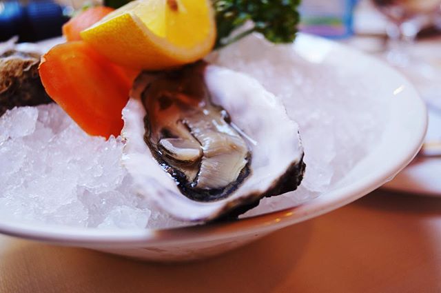 An oyster on ice with lemon wedge, presented in a close-up, shallow depth of field shot, perfect for a restaurant menu or food blog.