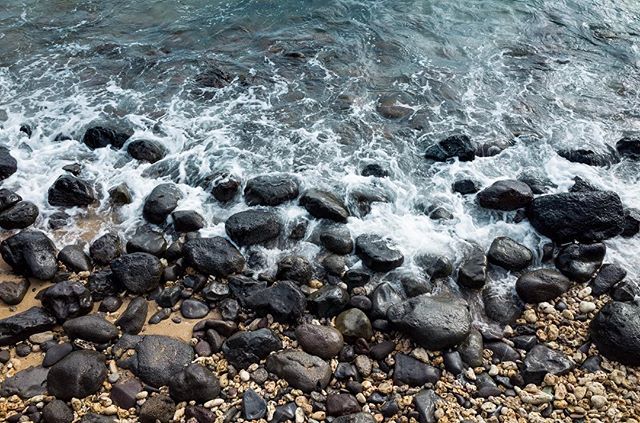 Waves wash over smooth rocks and pebbles on a serene beach, creating a peaceful coastal scene.