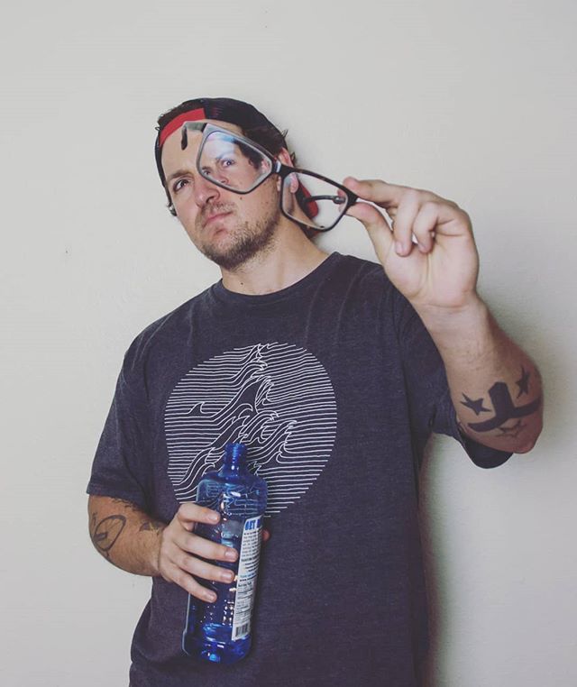 Man in t-shirt holds glasses and blue bottle for a fun, quirky studio shot.