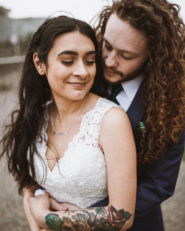A loving couple embraces on their wedding day, showcasing their bond and the tattoos on the bride's arm.
