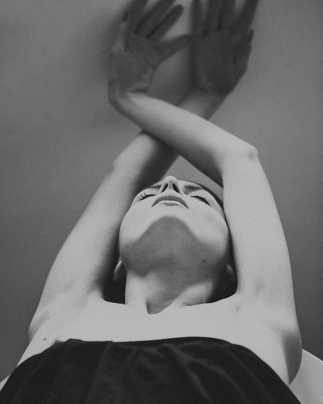 Black and white portrait of a woman with her arms crossed above her head looking up in a moment of peace and tranquility.