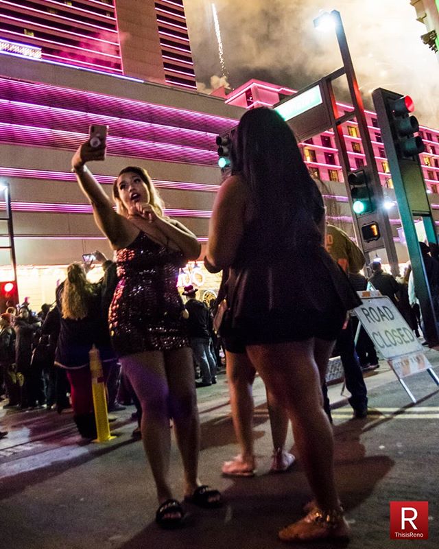 People celebrating outdoors at night with fireworks in the background in a city environment.