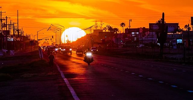 A city street at sunset featuring a motorcycle and other traffic illuminated by the vibrant colors of the setting sun.