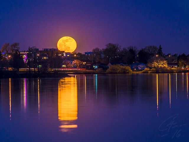 A full moon rises over a tranquil lake reflecting the city lights and creating a serene nightscape.