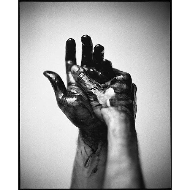 A monochrome image captures two hands covered in black paint, creating a conceptual and artistic visual.