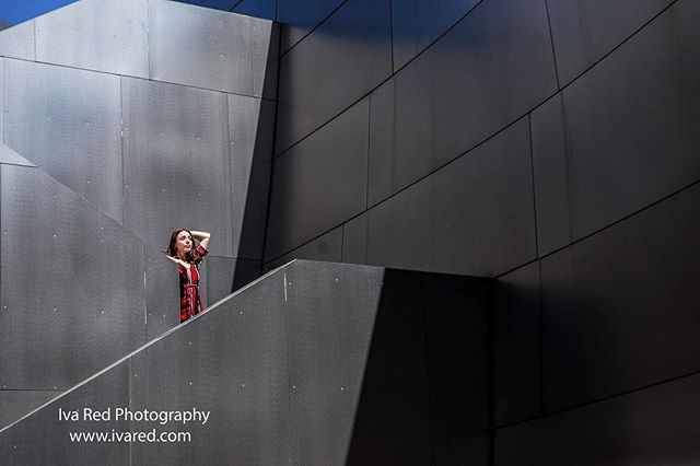 A woman in a red dress poses on a modern, gray architectural staircase in an urban setting.