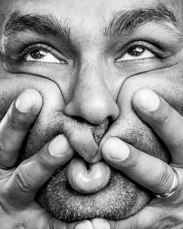 A close-up black and white portrait of a man playfully distorting his face with his hands.