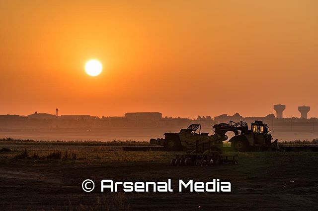 Construction equipment silhouettes against a vibrant sunrise, highlighting infrastructure and rural development.