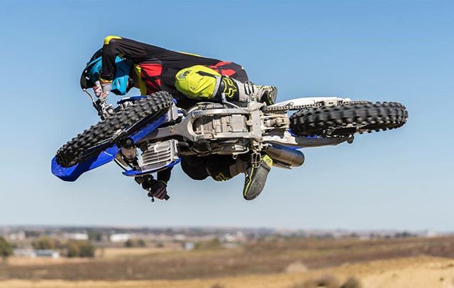 A motocross rider performs a jump with a dirt bike against a clear sky in an outdoor setting.