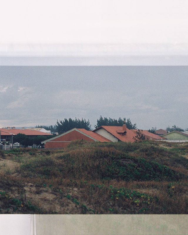 View of houses with red roofs surrounded by grassy dunes under a cloudy sky in a quiet residential area.