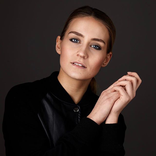 A woman with blue eyes poses in a studio wearing a black jacket. Simple, elegant portrait for beauty or lifestyle campaigns.