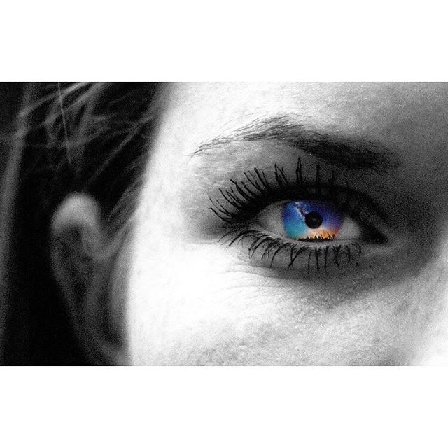 A striking close-up of an eye with a colorful iris against a monochrome face.