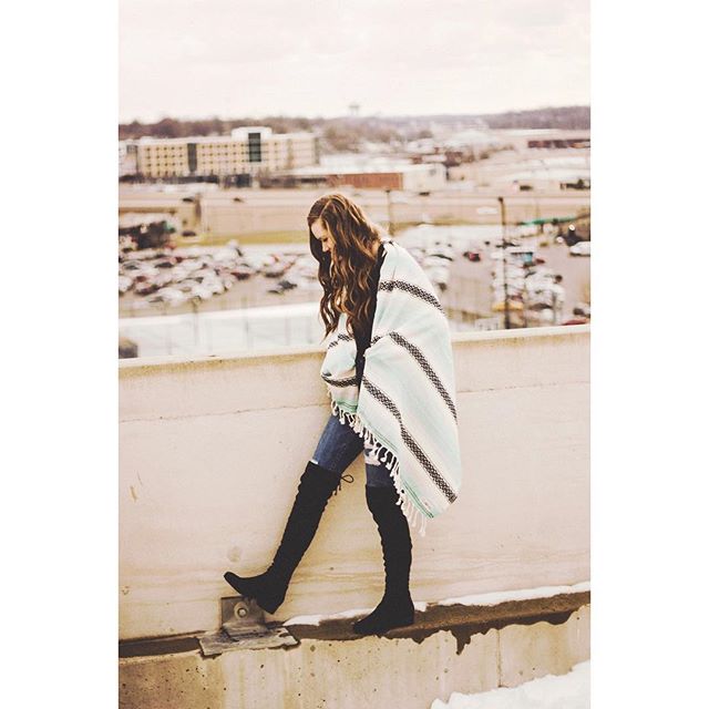 A woman in a poncho and thigh-high boots stands on a rooftop overlooking a cityscape.