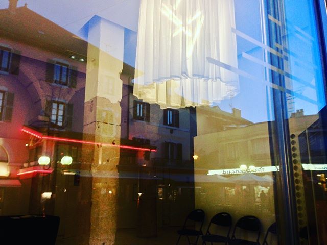 A window reflection shows a European city scene at night with a hanging lamp.