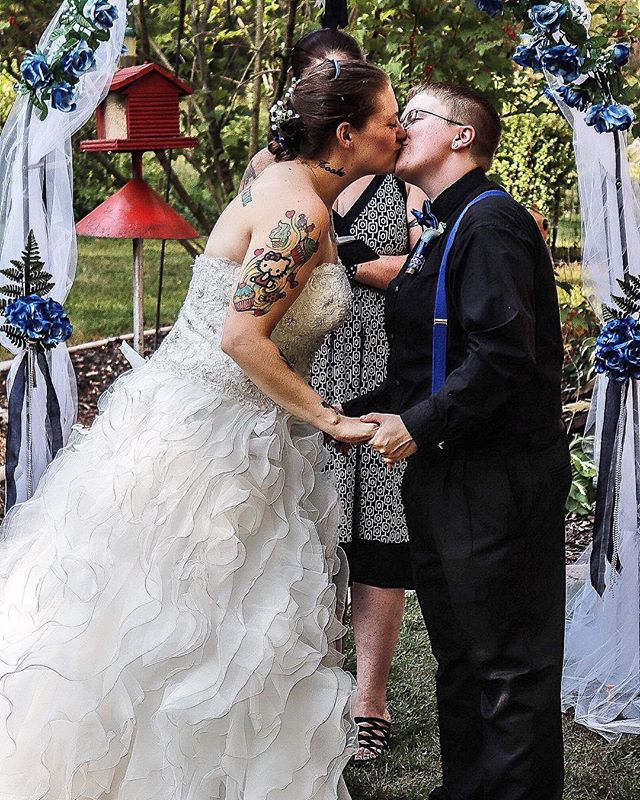 A lesbian couple shares a tender kiss during their outdoor wedding ceremony.