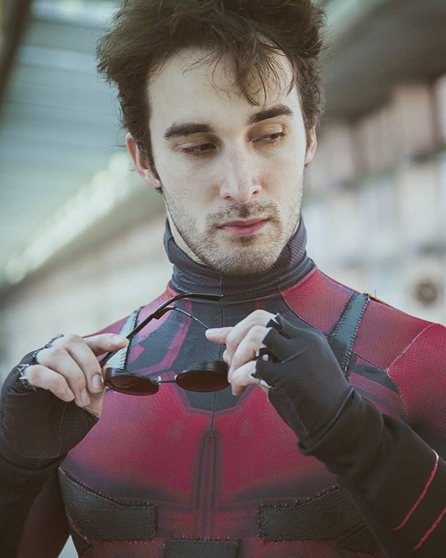 Man in daredevil cosplay adjusting sunglasses, showcasing a unique take on the superhero.